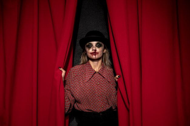 Mujer de maquillaje sosteniendo una cortina roja de teatro