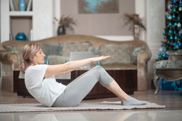 Una mujer de más de 50 años haciendo yoga en casa. Tendido en el suelo realiza ejercicios Asana. A una mujer le gusta el yoga.