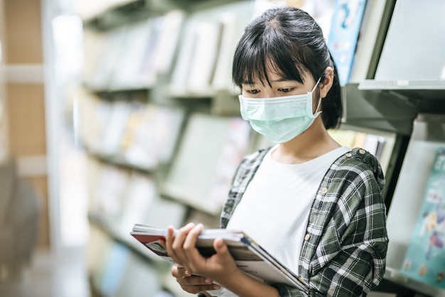 Una mujer con una máscara y buscando libros en la biblioteca.