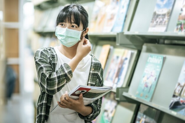 Una mujer con una máscara y buscando libros en la biblioteca.