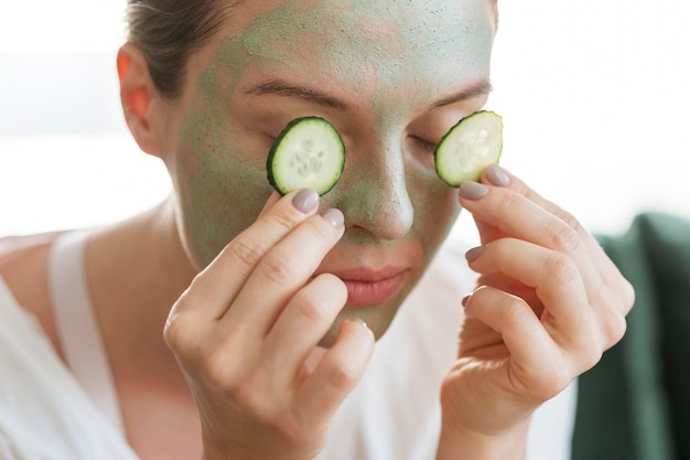 Mujer con máscara facial poniendo rodajas de pepino