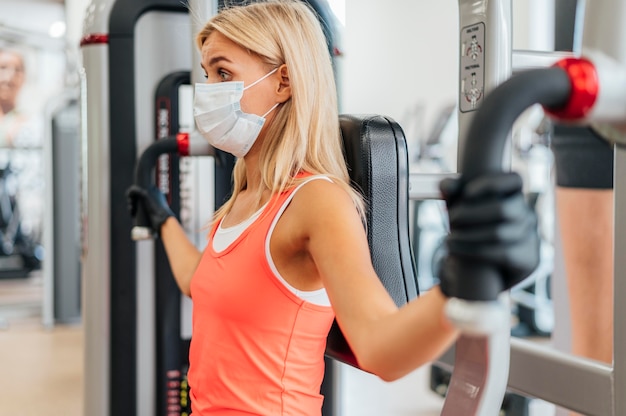 Mujer con máscara y guantes en el gimnasio haciendo ejercicio