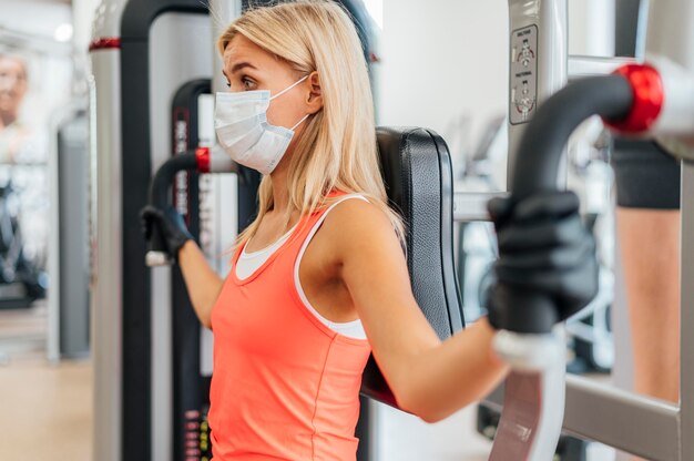 Mujer con máscara y guantes en el gimnasio haciendo ejercicio