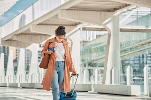 Mujer con máscara médica caminando con su equipaje en el aeropuerto durante la pandemia