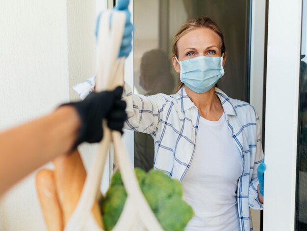 Mujer con máscara médica en casa recogiendo sus comestibles en autoaislamiento