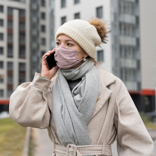 Mujer con máscara médica en la ciudad conversando por teléfono