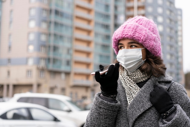 Mujer con máscara médica en la ciudad conversando por teléfono