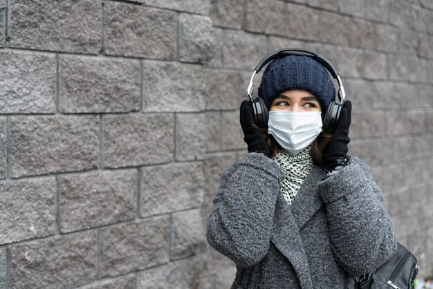 Mujer con máscara médica en la ciudad escuchando música con auriculares
