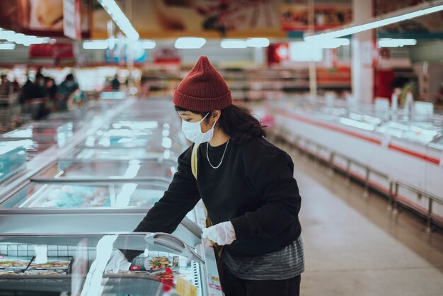 Mujer con máscara médica comprando comida congelada durante la pandemia de coronavirus