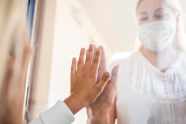 Mujer con máscara médica en cuarentena detrás de la ventana con el niño