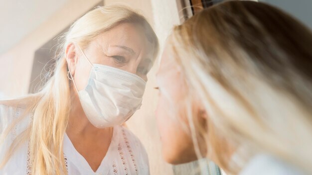 Mujer con máscara médica en cuarentena detrás de la ventana con niño