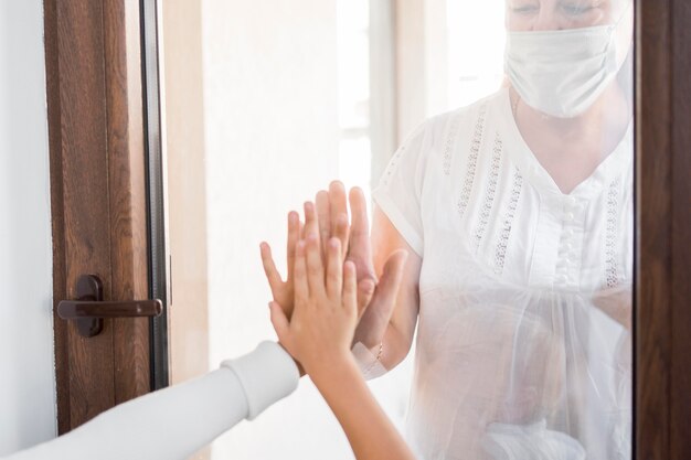 Mujer con máscara médica en cuarentena detrás de la ventana con personas