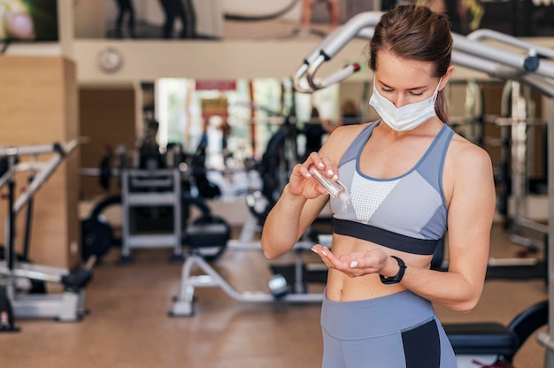 Mujer con máscara médica en el gimnasio con desinfectante de manos