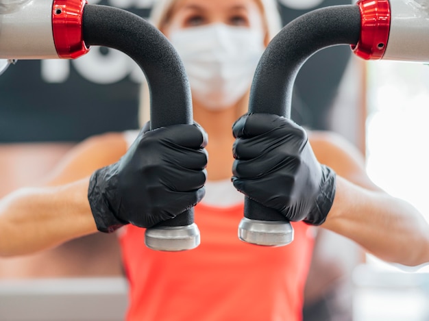 Foto gratuita mujer con máscara médica y guantes en el entrenamiento de gimnasio
