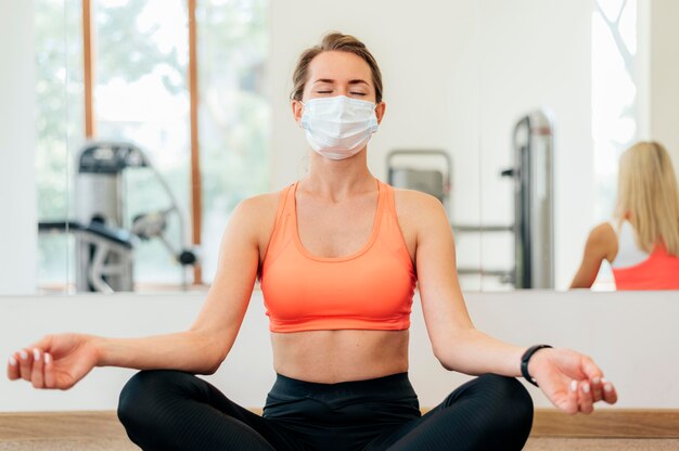 Mujer con máscara médica haciendo yoga en el gimnasio