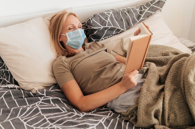 Mujer con máscara médica leyendo en cuarentena en casa