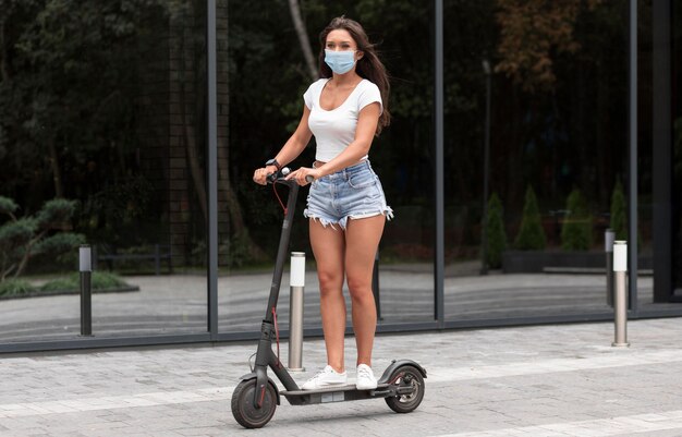 Mujer con máscara médica montando scooter eléctrico