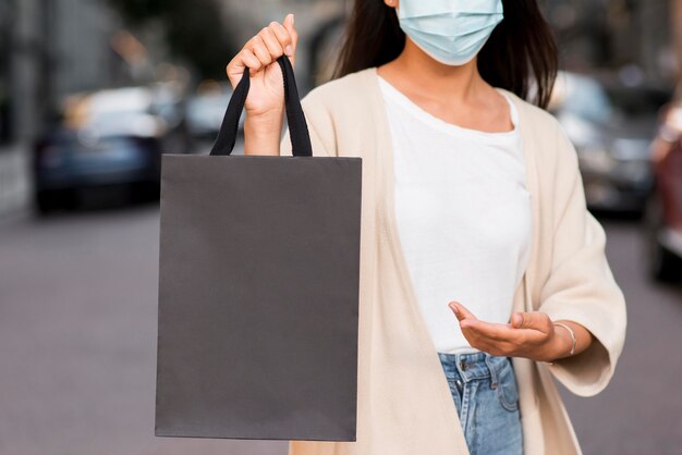 Mujer con máscara médica mostrando bolsa de compras que está sosteniendo