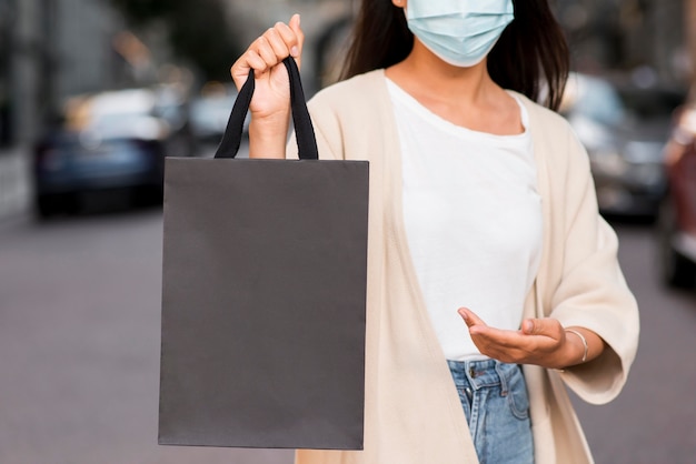 Mujer con máscara médica mostrando bolsa de compras que está sosteniendo