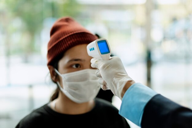 Mujer en una máscara médica obteniendo su temperatura medida por un termómetro electrónico