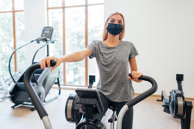 Mujer con máscara médica durante la pandemia haciendo ejercicio en el gimnasio