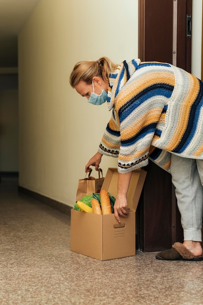 Foto gratuita mujer con máscara médica recogiendo sus alimentos en cuarentena