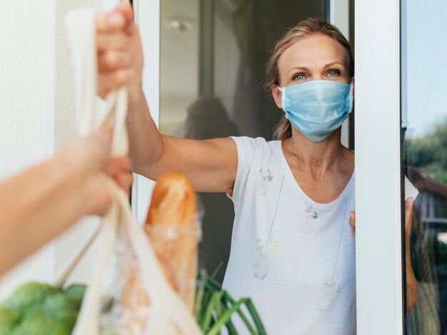 Mujer con máscara médica recogiendo sus comestibles en autoaislamiento