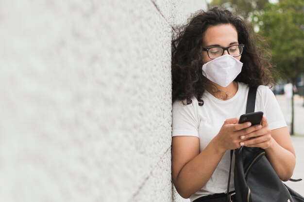 Mujer con máscara médica revisando su teléfono con espacio de copia