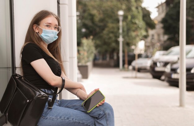Mujer con máscara médica sentada al aire libre