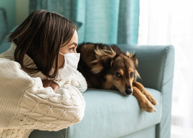 Mujer con máscara médica sentada junto a su perro en casa durante la pandemia