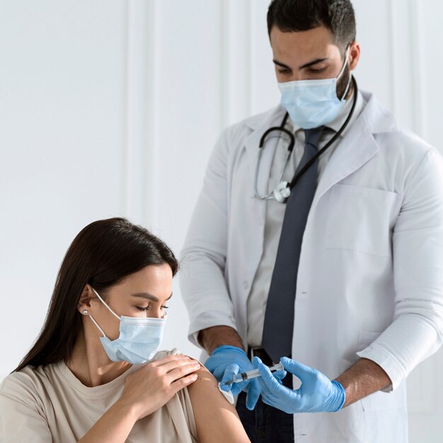 Mujer con máscara médica siendo vacunada por médico