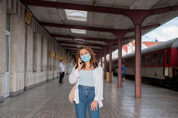 Mujer con máscara médica con smartphone en la estación de tren pública