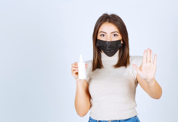 Mujer con una máscara médica sosteniendo un spray y haciendo señal de stop.