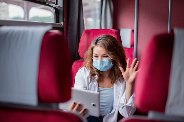 Foto gratuita mujer con máscara médica con tableta para videollamadas mientras viaja en tren público