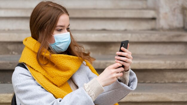 Mujer con máscara médica tomando fotografías con smartphone