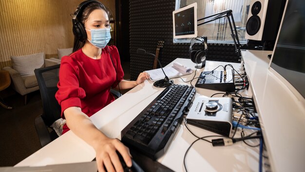 Mujer con máscara médica trabajando en radio con equipo profesional