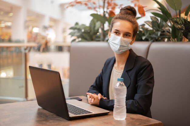 Mujer con máscara médica trabajando en su computadora portátil