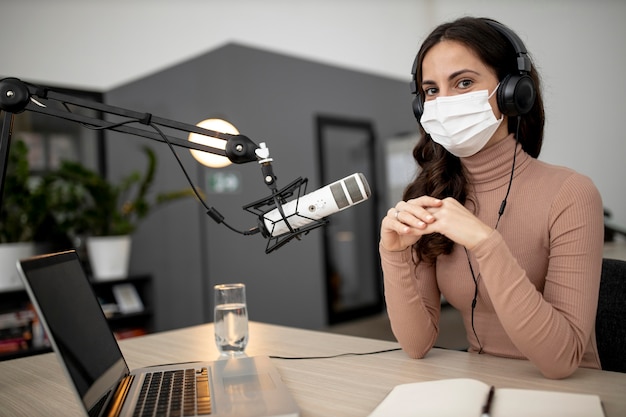 Mujer con máscara médica transmitiendo en radio con micrófono