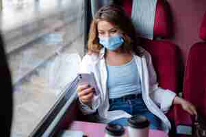 Foto gratuita mujer con máscara médica viajando en tren público y usando smartphone