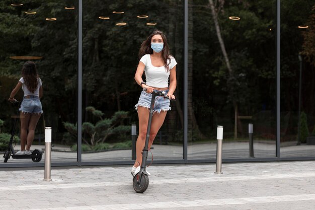 Mujer con máscara montando un scooter eléctrico