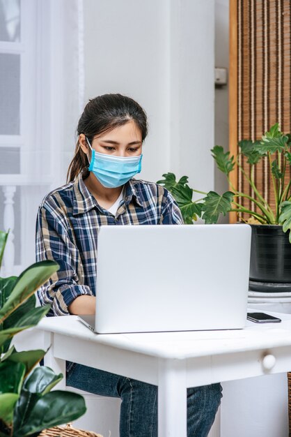 Una mujer con una máscara usa una computadora portátil para trabajar.