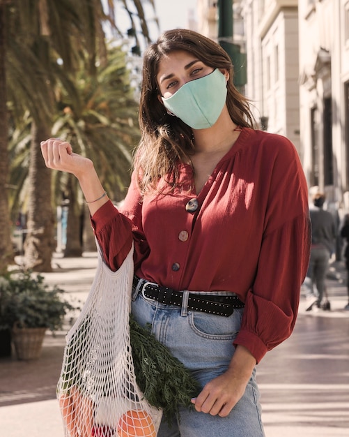 Foto gratuita mujer con mascarilla al aire libre con bolsa de supermercado