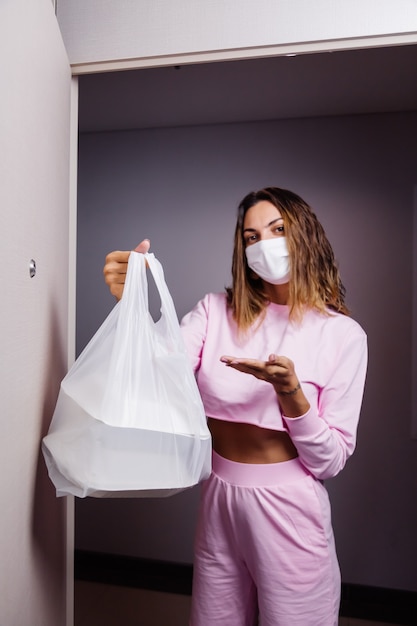 Mujer con mascarilla blanca médica recibe una bolsa de plástico con comida de un repartidor