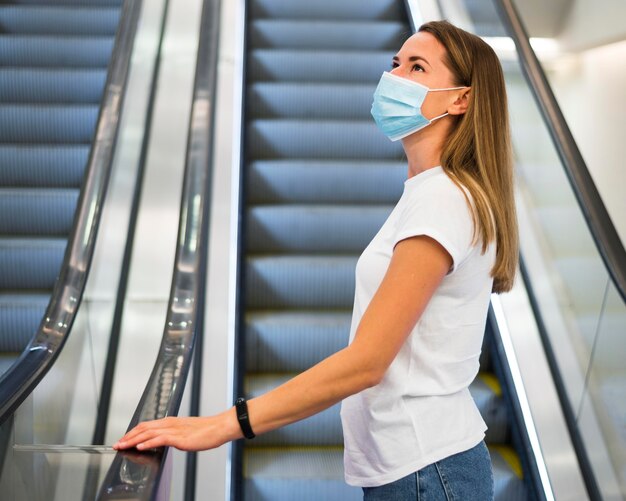 Mujer con mascarilla en la escalera mecánica