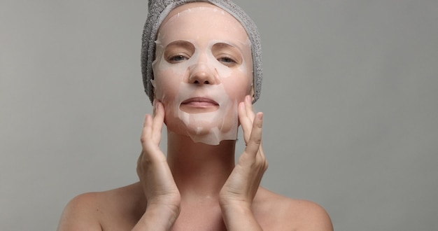 Una mujer con una mascarilla facial se hace un masaje facial