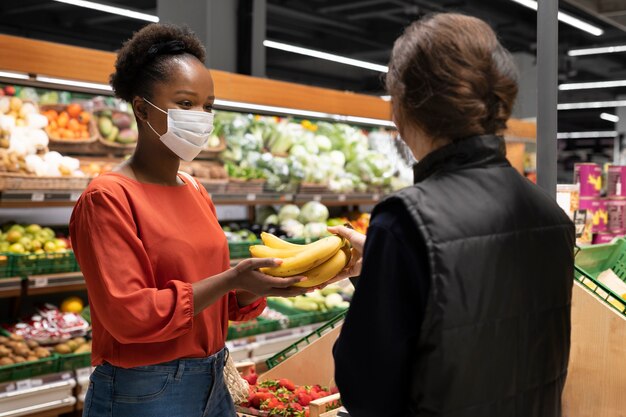Mujer con mascarilla médica pidiendo plátanos en el supermercado