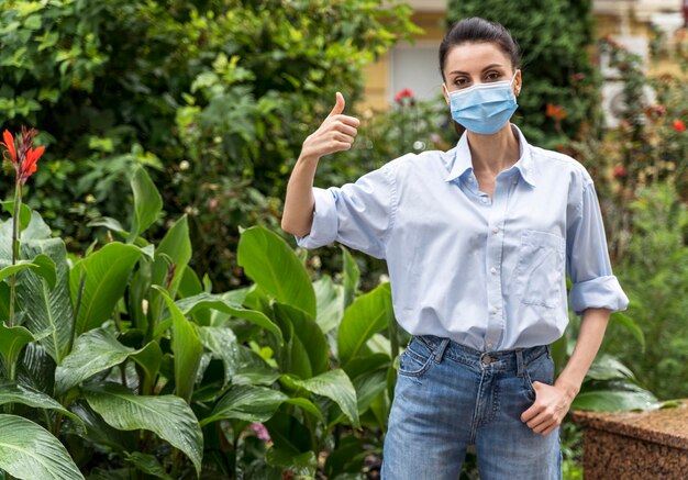 Mujer con mascarilla mostrando el pulgar hacia arriba firmar con espacio de copia