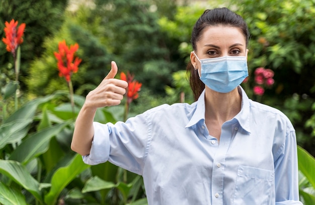 Foto gratuita mujer con mascarilla mostrando el pulgar hacia arriba signo