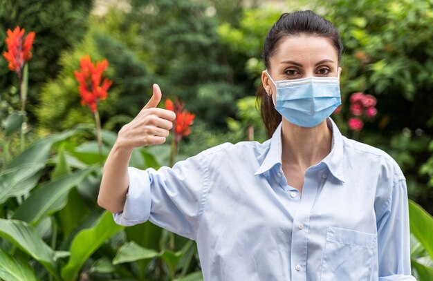 Mujer con mascarilla mostrando el pulgar hacia arriba signo