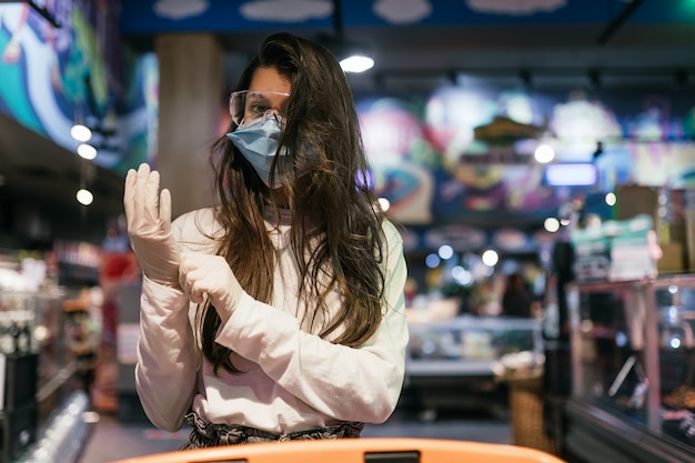 Mujer con mascarilla quirúrgica y guantes está comprando en el supermercado.